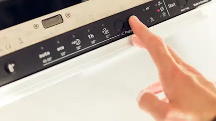 Hand drückt auf eine Taste in der Bedienleiste des Geschirrspülers