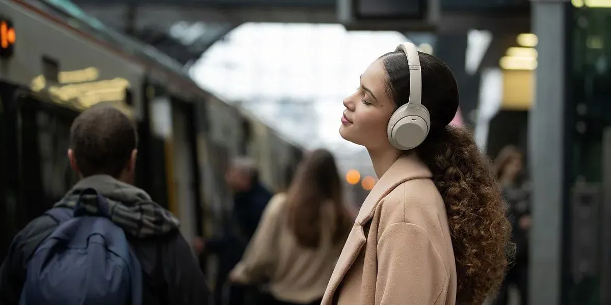 Eine Frau hört Musik mit beigen Over-Ear-Kopfhörern in einem öffentlichen Verkehrsmittel.