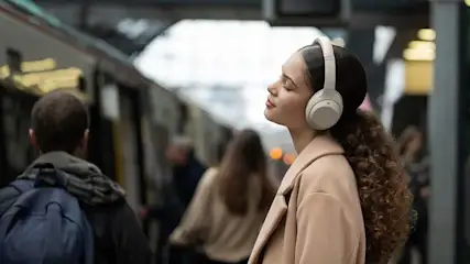 Eine Frau hört Musik mit beigen Over-Ear-Kopfhörern in einem öffentlichen Verkehrsmittel.