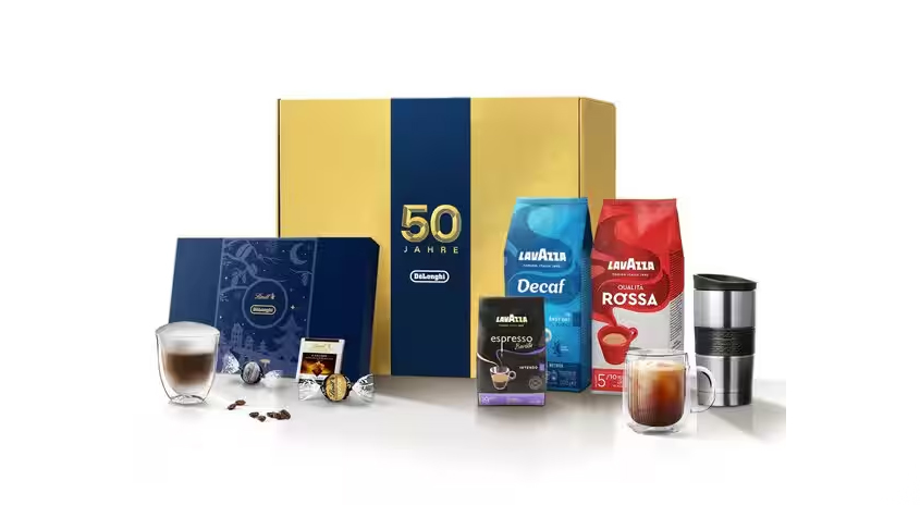 Eine goldene Box mit Kaffeepackungen, Tassen, Kaffeebohnen und Schokolade auf einem weißen Tisch.