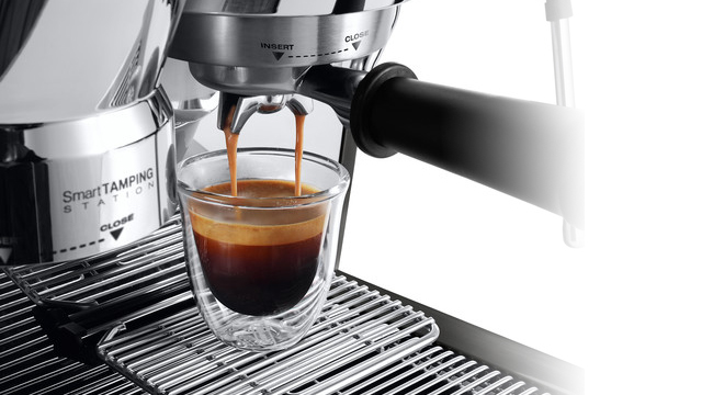 Ein Espresso läuft in ein Glas unter einer silbernen Espressomaschine auf einem Metallrost.