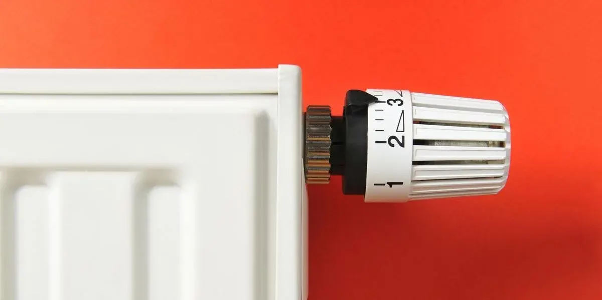 Ein weißer Heizkörper mit einem weißen Thermostatventil, eingestellt zwischen 2 und 3, ist vor einer roten Wand zu sehen.