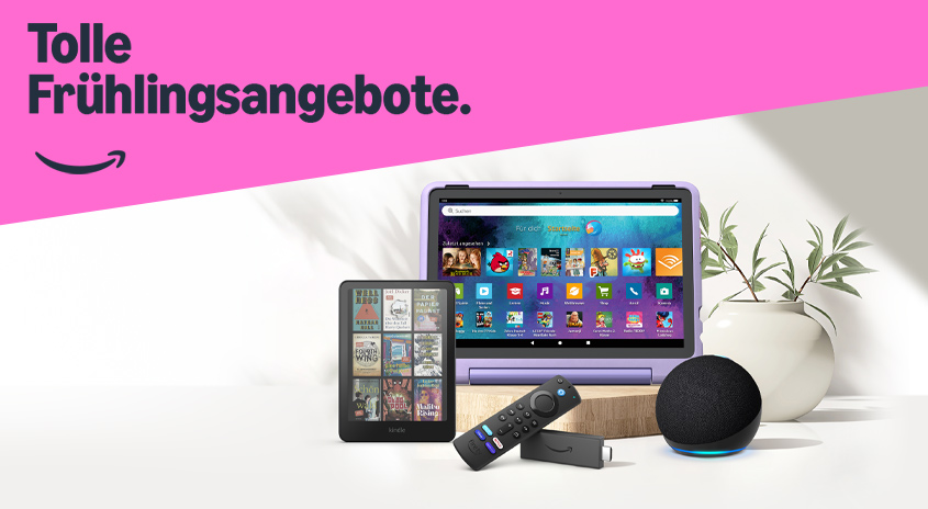 Auf einem Tisch liegen ein Tablet, ein E-Reader, eine Fernbedienung, ein Fire TV Stick und ein Echo Dot vor einer Pflanze.