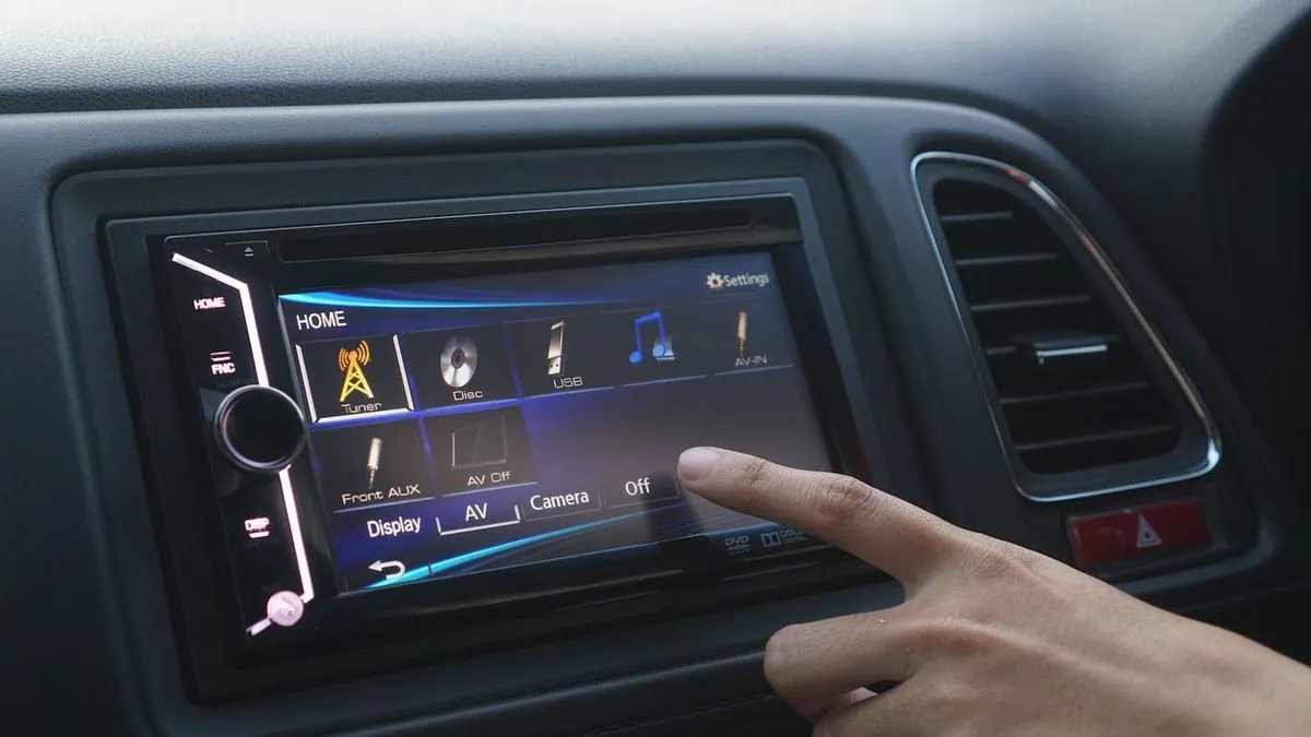Finger tippt auf den Touchscreen eines modernen Autoradios mit verschiedenen Medienoptionen