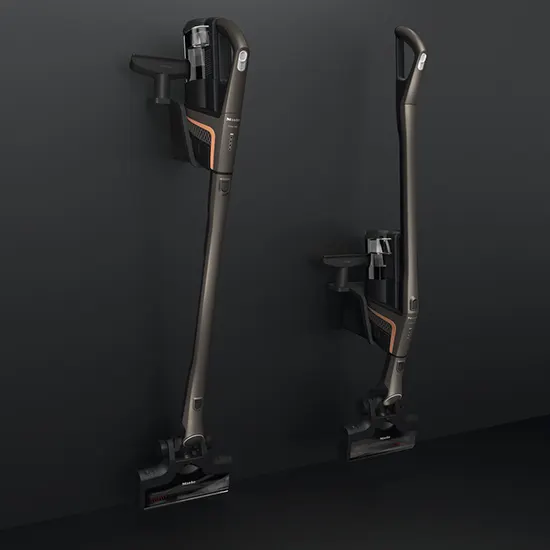 Zwei kabellose Staubsauger, einer an der Wandhalterung, vor einem dunklen Hintergrund.