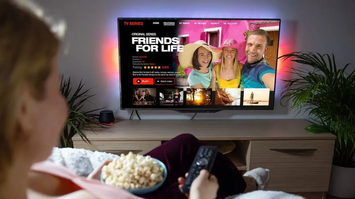 Eine Person schaut TV, hält Popcorn und Fernbedienung. Auf dem Bildschirm läuft die Serie 'Friends for Life'.