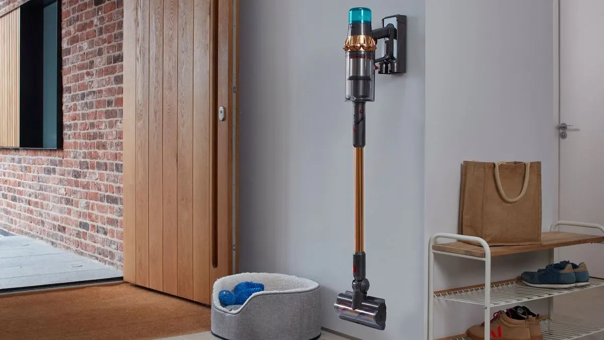 Dyson Gen5detect Akku-Staubsauger hängt an einer Wandhalterung im Flur neben einer Schuhbank, einem Korb und einem Hundebett..