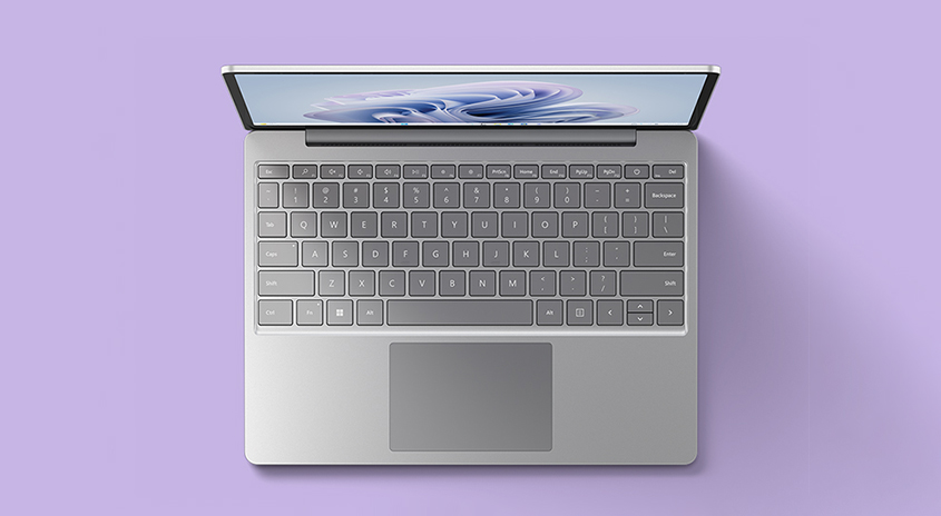 Silberner Laptop mit Tastatur auf lila Hintergrund. Der Bildschirm ist leicht geöffnet und zeigt ein abstraktes Muster.