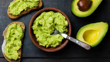 Avocadoaufstrich in der Schüssel und damit bestrichene Brote