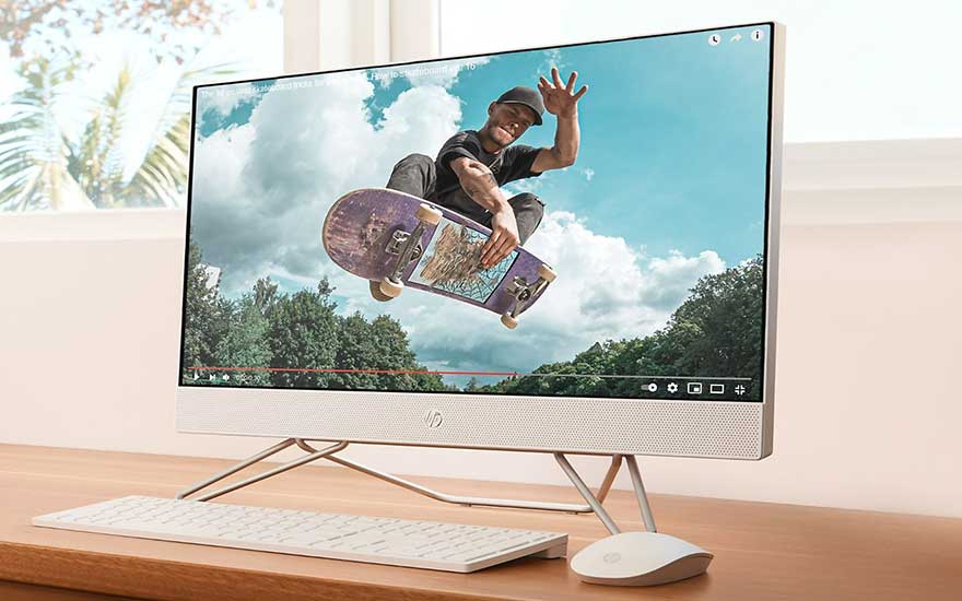 Un ordinateur tout-en-un blanc affiche une vidéo de skateboard sur un bureau en bois avec un clavier et une souris blancs.