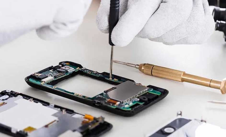 Un smartphone noir est démonté sur une surface blanche, avec un tournevis noir et un tournevis doré à proximité.