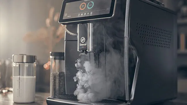 Machine à café Saeco noire avec écran, émettant de la vapeur. Bocal en verre rempli de liquide blanc visible à côté.