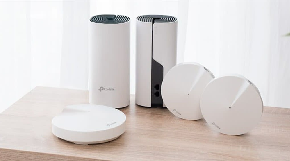 Deux routeurs blancs cylindriques et trois routeurs circulaires blancs sur une table en bois.