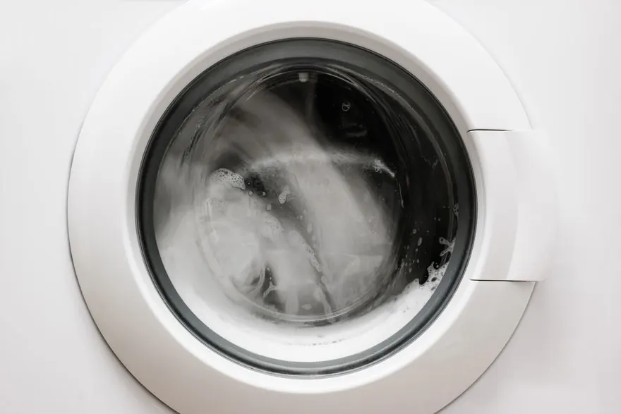 Een witte wasmachine met een ronde deur in bedrijf, gevuld met water en kleding in beweging.