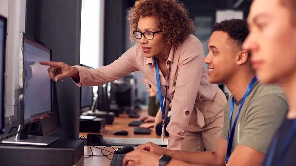 Une salle informatique avec des ordinateurs sur des bureaux en bois. Un écran d'ordinateur est pointé par une main.