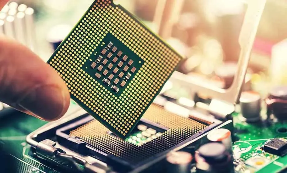 Een computerprocessor wordt boven een groene printplaat gehouden. De processor is vierkant en bedekt met kleine gouden contactpunten.