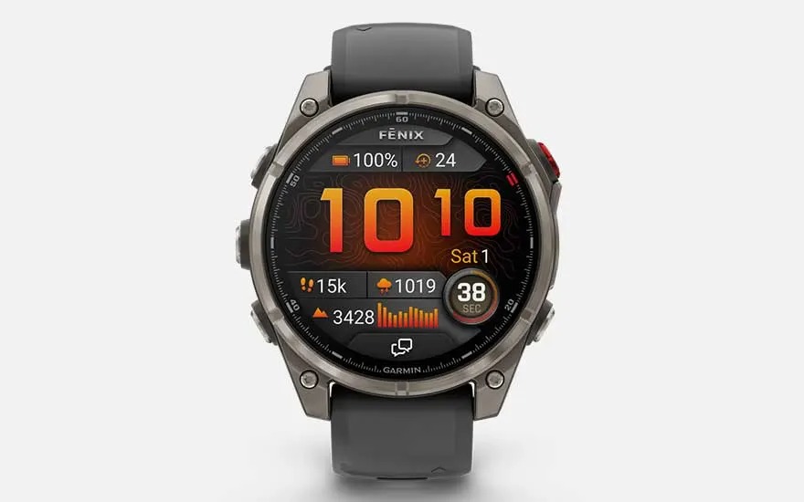 Une montre Garmin Fenix à écran rond affiche l’heure, la date, la batterie, les pas, la fréquence cardiaque, les notifications et la météo.
