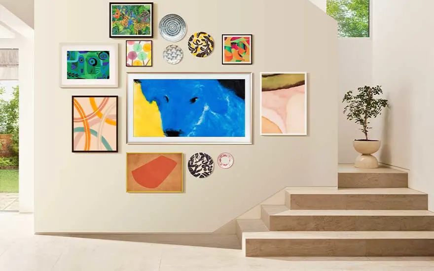 Een elegante woonkamer met een grote ingelijste TV aan de muur, omringd door kunstwerken. Een vrouw zit en drinkt koffie bij het raam.