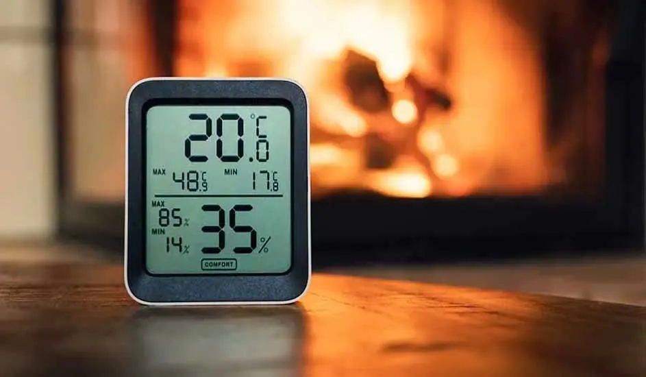 Een digitale thermometer geeft 20.6°C en 35% luchtvochtigheid weer, voor een vage achtergrond met een open haard.