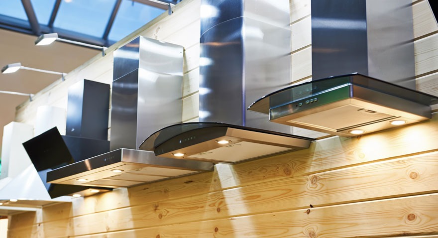 Rangée de hottes de cuisine en acier inoxydable et noires montées sur un mur en bois clair. Luminaires visibles au plafond.