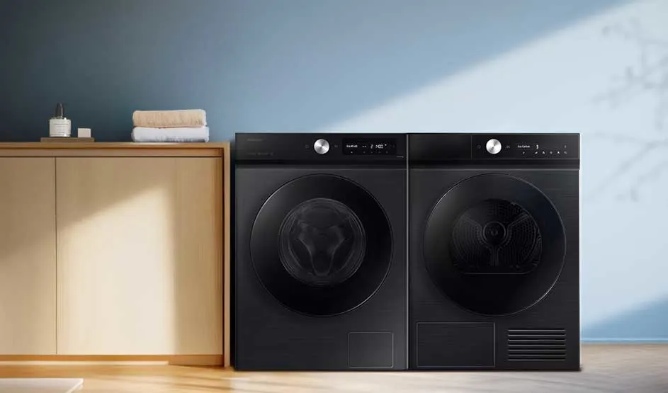 Twee zwarte wasmachines naast een lichte kast met handdoeken; blauwe muur met zonlichtschuine schaduw, rustige minimalistische washoek.