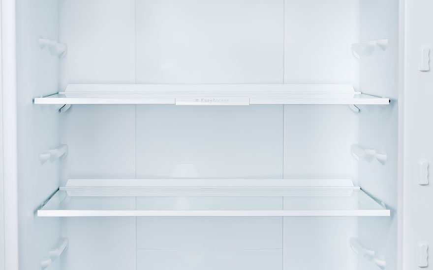 Vue intérieure d'un réfrigérateur blanc vide avec deux étagères en verre transparent.