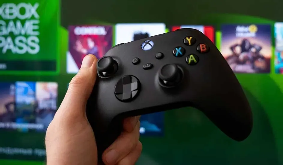 Une main tient une manette Xbox noire, avec en arrière-plan le menu Xbox Game Pass et plusieurs jaquettes de jeux.