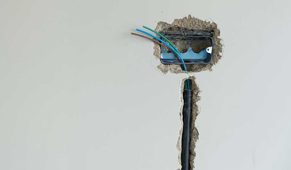 Boîte électrique murale apparente avec fils bleu, brun et vert. Conduit noir vertical en dessous.