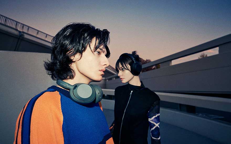 Deux jeunes portant des casques élégants posent dehors au crépuscule, leurs tenues modernes s’accordent au décor urbain.