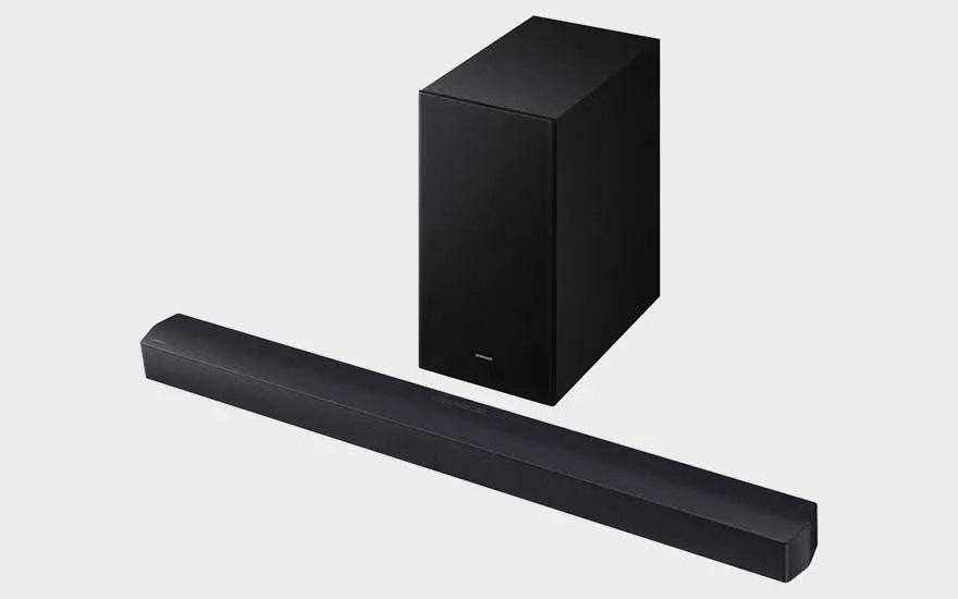 Een zwarte Samsung soundbar en een grote subwoofer worden samen getoond op een lichte achtergrond, in een sobere productpresentatie.