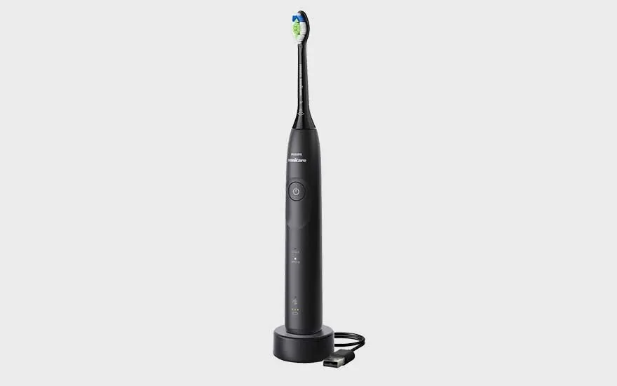 A black Philips electric toothbrush stands on its charger with a USB cable, set against a plain background.