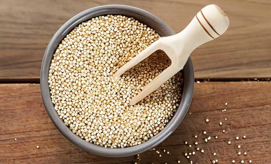 Un bol gris rempli de quinoa blanc est posé sur une table en bois avec une cuillère en bois.