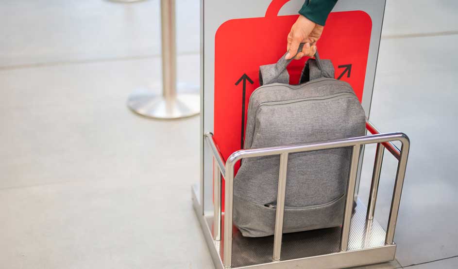 Un sac à dos gris dans un chariot métallique devant un panneau rouge avec des flèches noires pointant vers le haut.