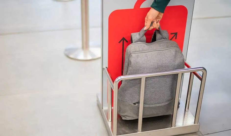 Un sac à dos gris dans un chariot métallique devant un panneau rouge avec des flèches noires pointant vers le haut.