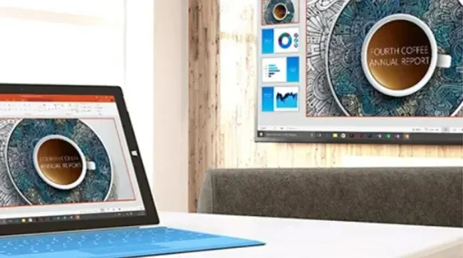 Een blauwe laptop en een monitor tonen een rapport met een kop koffie op een wit bureau.