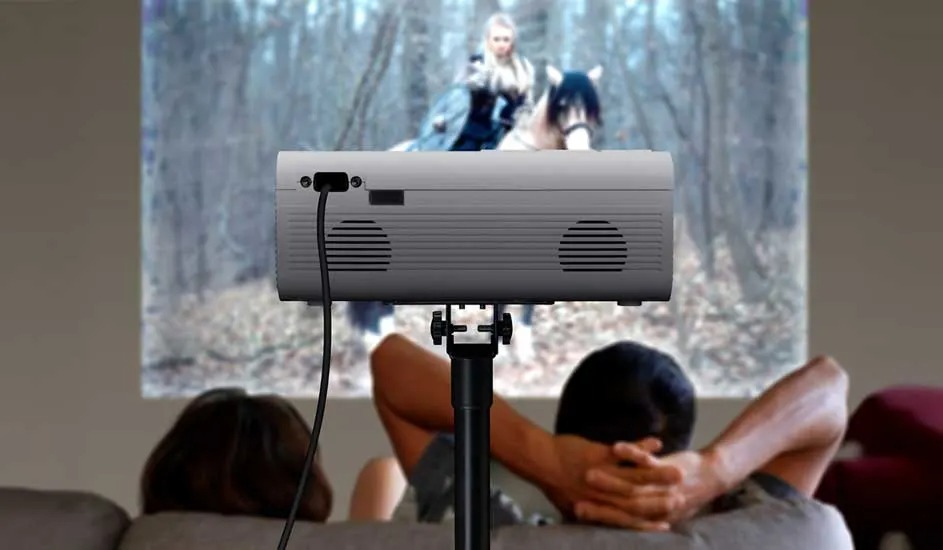 Twee mensen zitten ontspannen op een bank en kijken naar een film die via een projector op de muur wordt geprojecteerd. Geen merk is zichtbaar.