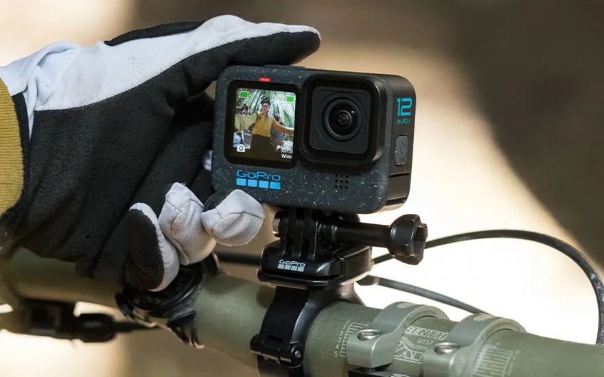 Black GoPro camera mounted on a green bicycle handlebar with a gloved hand nearby.