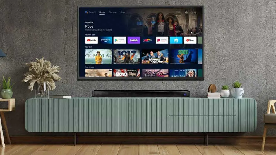 Un téléviseur affiche des films sur un meuble vert avec des plantes et une décoration sur un sol en bois.