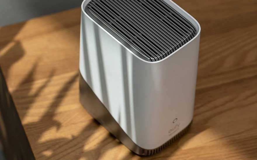 Un purificateur d'air blanc et gris avec des grilles sur le dessus, sur une table en bois avec des ombres.