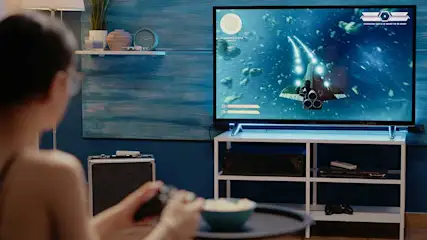 Een tv toont een ruimteschip in een blauwe ruimte. Een witte plank met decoratie hangt aan de muur. Voor de tv staat een witte kast.