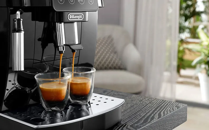 Een zwarte DeLonghi-espressomachine schenkt koffie in twee glazen. De machine staat op een donker houten oppervlak.
