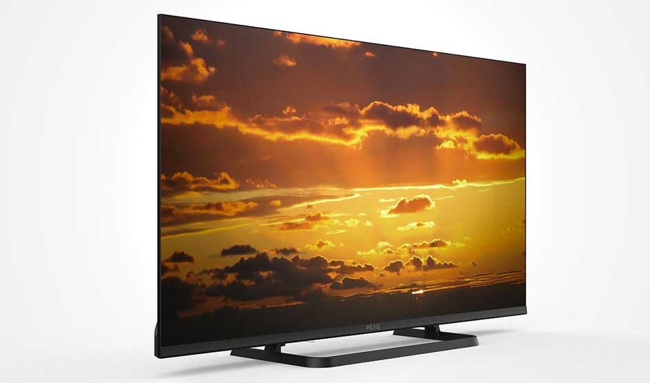 Un téléviseur PEAQ affiche un coucher de soleil éclatant avec des nuages orange et jaunes, posé sur un support noir sur fond blanc.