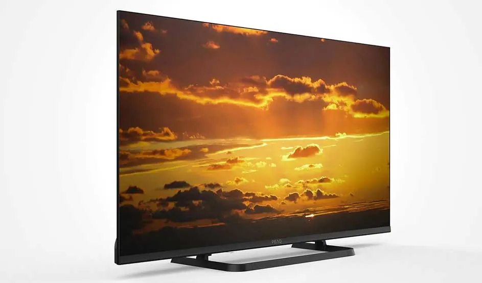 Un téléviseur PEAQ affiche un coucher de soleil éclatant avec des nuages orange et jaunes, posé sur un support noir sur fond blanc.