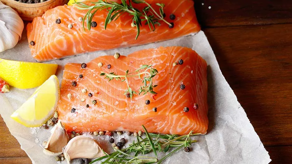 Twee stukken zalm op papier met citroen, look en kruiden. De achtergrond is donker hout.