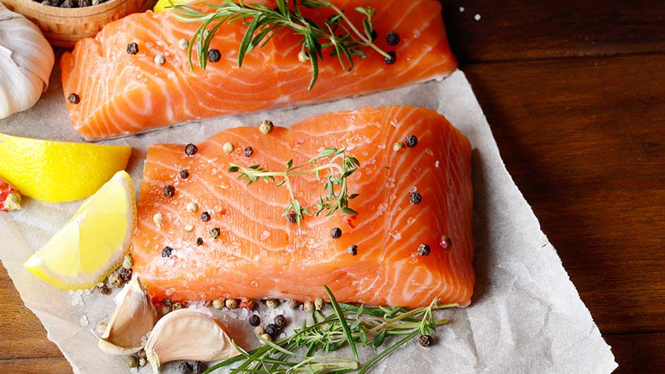 Deux filets de saumon orange vif sur papier, assaisonnés de poivre, citron, ail et herbes. Sur fond de bois.