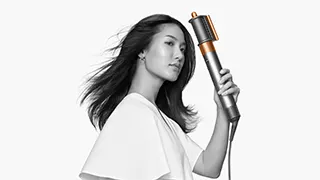 Een zilveren en gouden Dyson Airwrap vasthoudend, tegen een witte achtergrond.