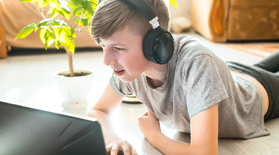 Een laptop op een witte vloer, met een groene plant in een witte pot. Zwarte hoofdtelefoon ligt ernaast.
