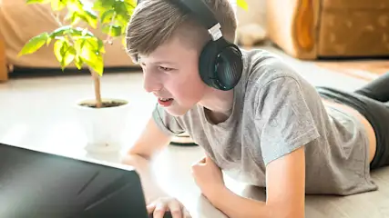 Een laptop op een witte vloer, met een groene plant in een witte pot. Zwarte hoofdtelefoon ligt ernaast.