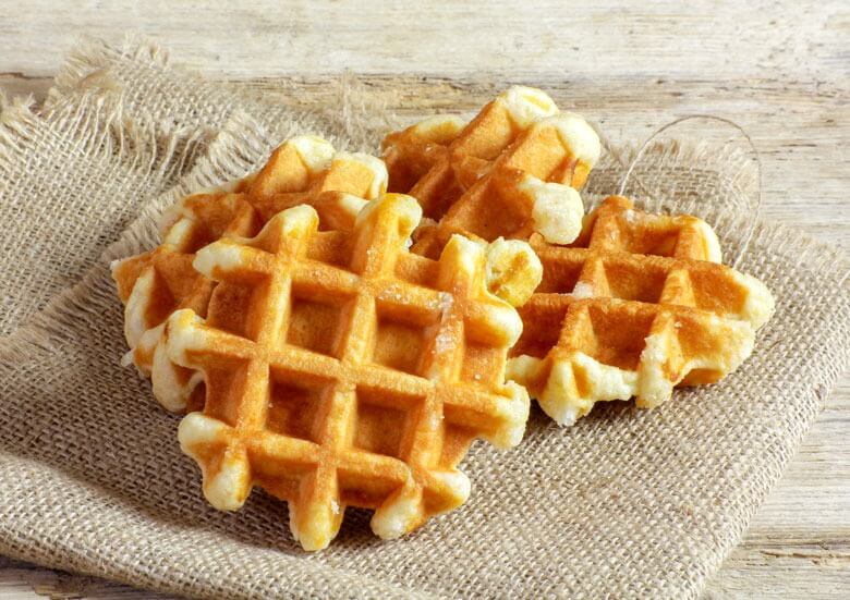 Gestapelde goudbruine wafels op een beige linnen doek, met een houten achtergrond.