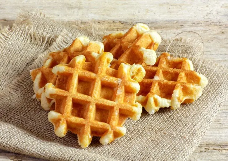 Gestapelde goudbruine wafels op een beige linnen doek, met een houten achtergrond.
